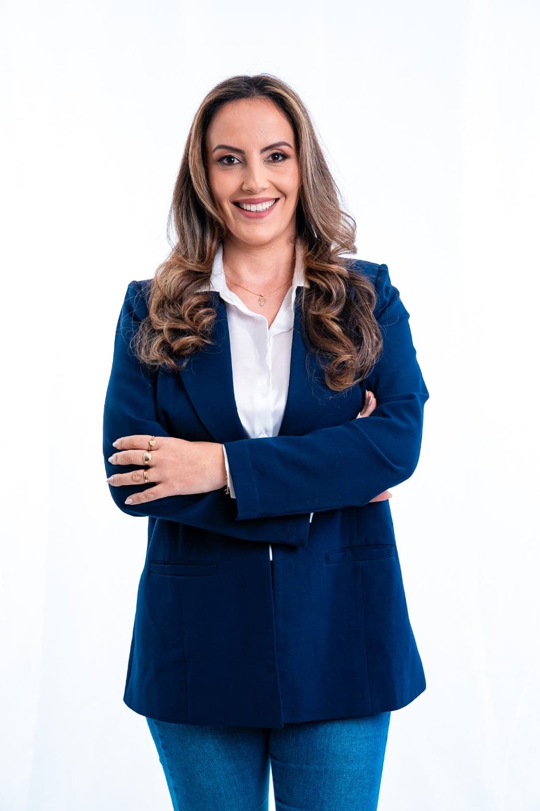 Michele Marques de blazer azul e camisa branca, de braços cruzados, em fundo branco